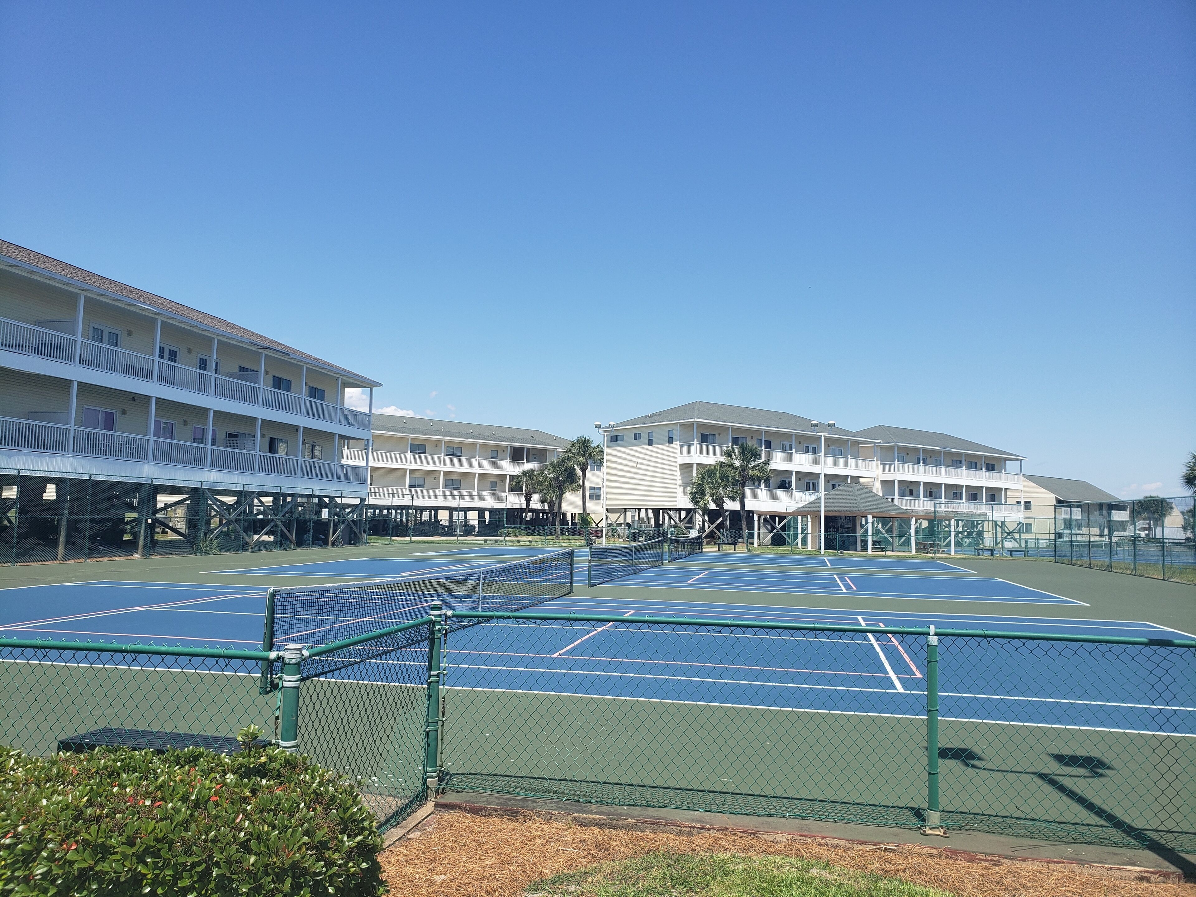 Un court de tennis avec un filet, entouré d’une clôture en treillis métallique.