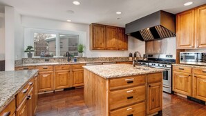 Une cuisine moderne avec des meubles en bois, des comptoirs en granit, une cuisinière en acier inoxydable et un grand îlot central doté de tiroirs.