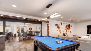 Une table de billard dans une pièce qui comprend un coin repas, un canapé et un mur orné d’une carte.
