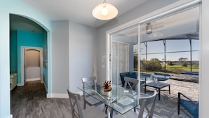 A modern dining area with a glass table and chairs, a ceiling fan, and a view of a swimming pool and outdoor space. - Beautiful Pool Home with Spa & Games Room in Golf Community Close to Disney (Davenport)