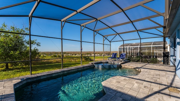 A covered outdoor swimming pool with clear blue water, surrounded by a metal frame and a stone patio. - Beautiful Pool Home with Spa & Games Room in Golf Community Close to Disney (Davenport)