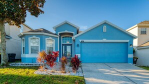 A two-story house with a blue garage and a front yard with small trees. - Beautiful Pool Home with Spa & Games Room in Golf Community Close to Disney (Davenport)