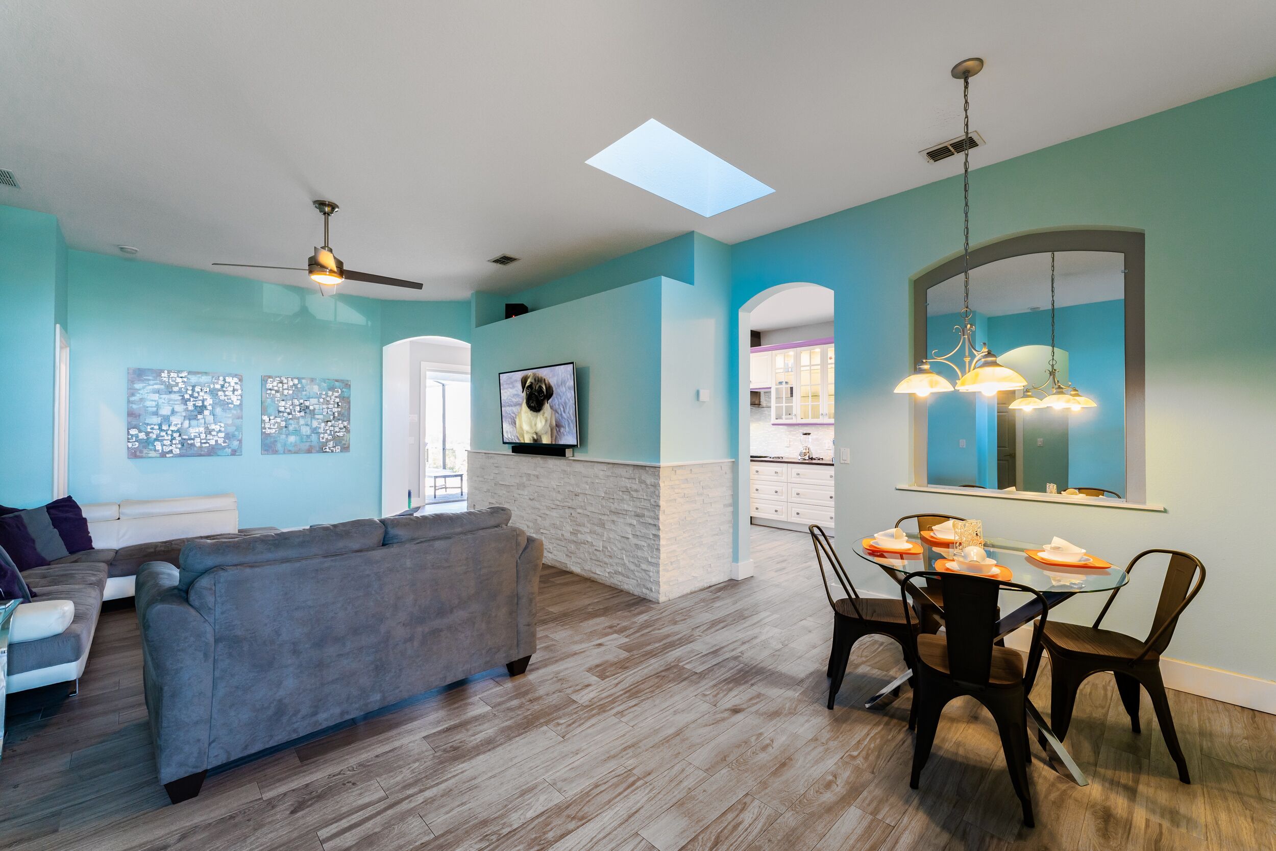 Un salon moderne avec un canapé gris, une table à manger avec des chaises et un ventilateur de plafond.