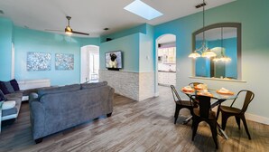 A modern living room with a gray sofa, a dining table with chairs, and a ceiling fan. - Beautiful Pool Home with Spa & Games Room in Golf Community Close to Disney (Davenport)