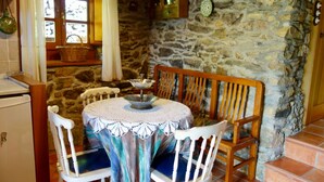 A rustic dining area with a round table, white chairs, and a stone wall backdrop.