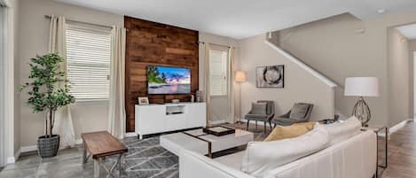 Una sala de estar moderna con un sofá blanco, una mesa de centro, un televisor en una pared de madera, una planta en maceta y una escalera.