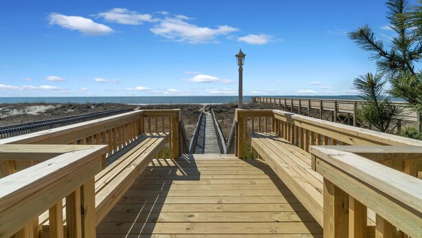 Eine Holzpromenade führt zu einem Strand, in der Ferne steht eine Laterne.