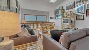 Ein geräumiges Wohnzimmer mit großem Fenster, Deckenventilator und verschiedenen gerahmten Bildern an den Wänden.