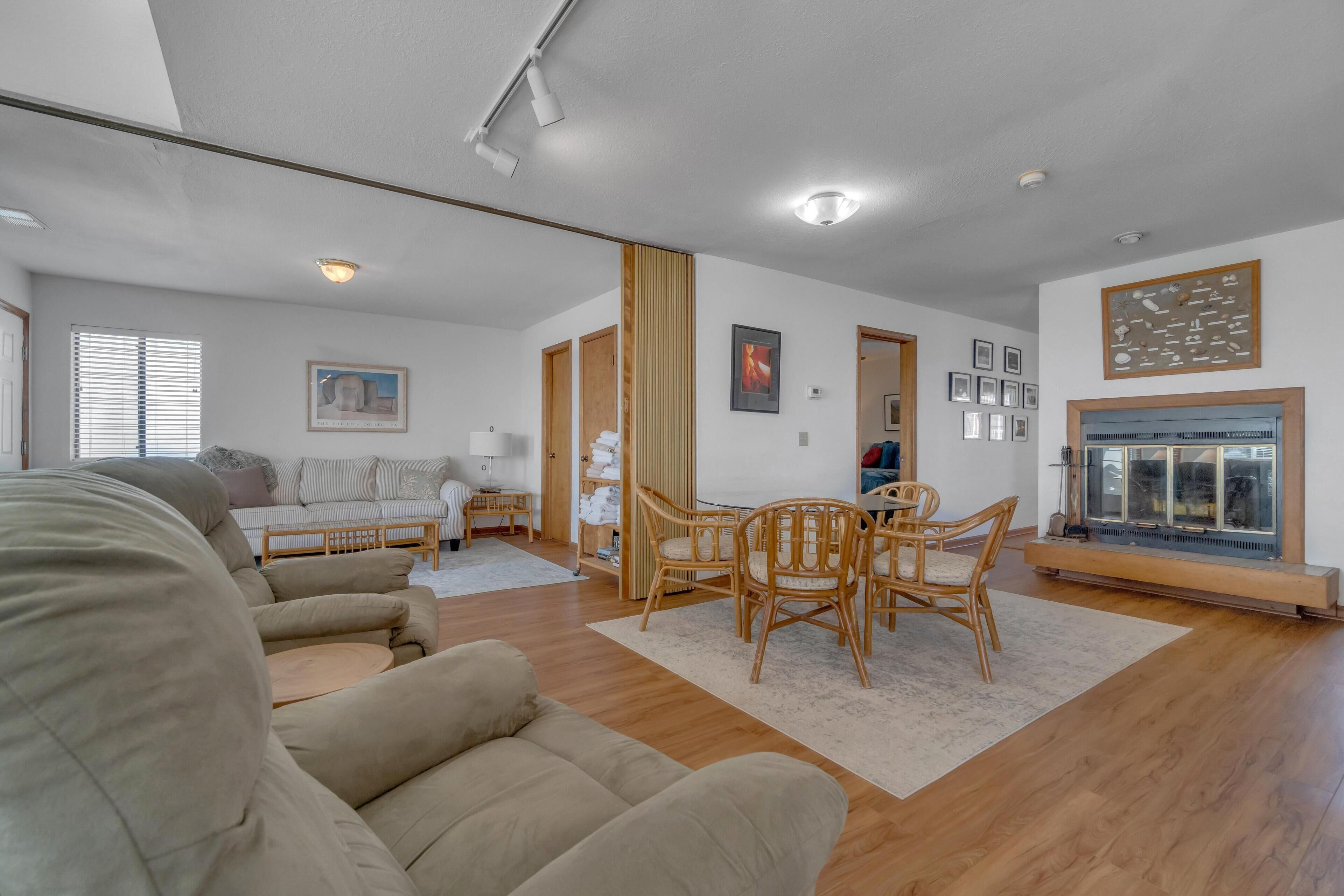 A modern living room with a sofa, a dining table with chairs, a fireplace, and a collection of framed pictures on the wall.