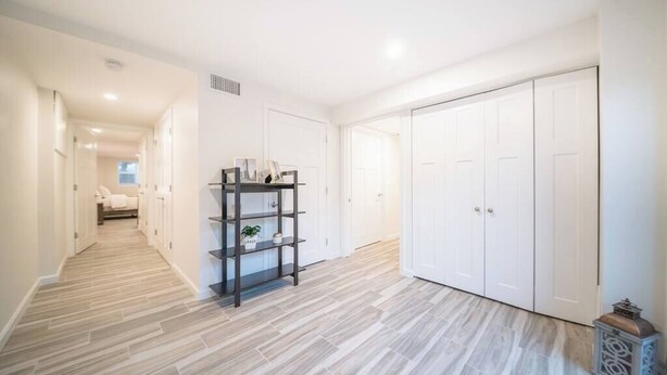A hallway with a wooden floor, white walls, and a black shelving unit with decorative items.