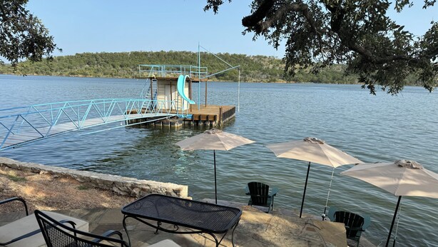 Un pontile sul lago con una piccola piattaforma, arredi da esterno con sedie e tavoli, e ombrelloni.