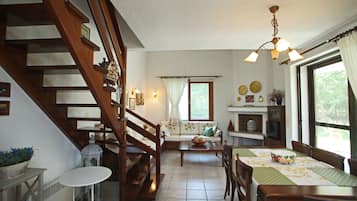 Un salon chaleureux avec un escalier en bois, un coin repas avec une table et des chaises, et une cuisine avec une fenêtre et des rideaux.