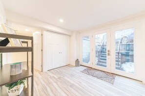 Amplia habitación con piso de madera, una puerta blanca y un ventanal con vistas a una escalera.