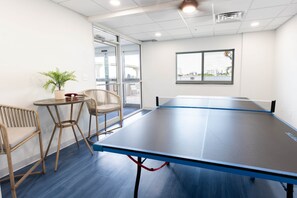 A ping pong table in a room with a view of a cityscape through a window.