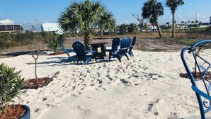 A sandy outdoor area with a table and chairs, surrounded by palm trees and a few buildings in the background. - Shuckers & Beaches!  In Beautiful Mexico Beach, FL (Mexico Beach)