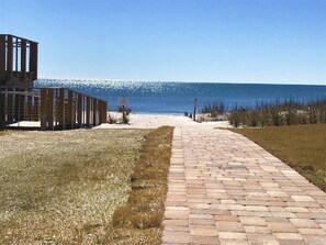 Un sentier mène à une plage, avec une structure en bois sur la gauche.