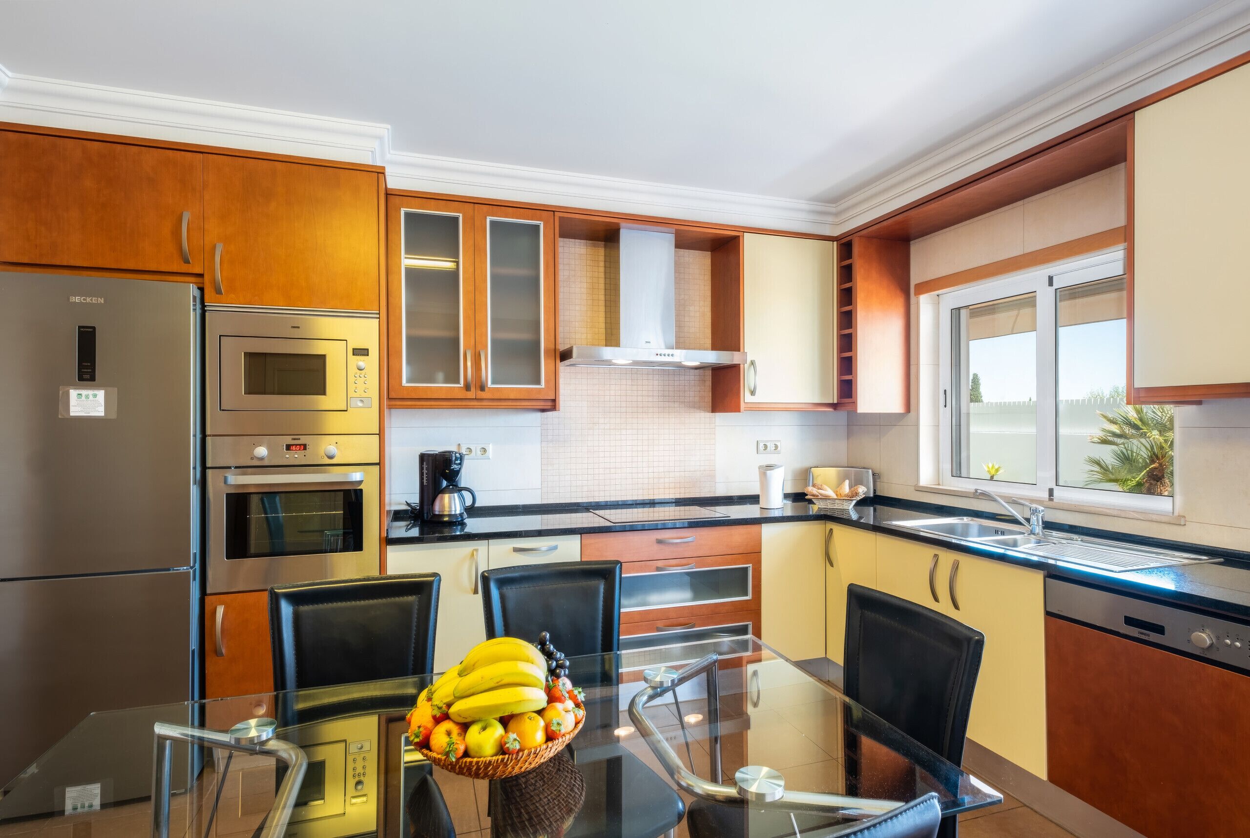 A modern kitchen with stainless steel appliances, a glass dining table, and a view of the outdoors.