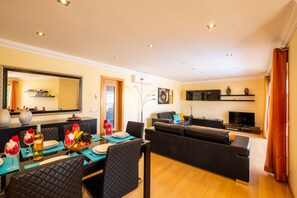 Uma sala de estar moderna com um sofá, um espaço de jantar com mesa posta para dois e uma TV de tela plana na parede.