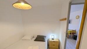 Ein Schlafzimmer mit Bett, Kissen, einem Nachttisch mit Lampe, einem Fenster und Blick auf einen Essbereich.