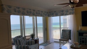 A room with a view of the beach, a ceiling fan, striped furniture, and a dining table with a bowl. - Crescent Arms Luxurious Gulf front Siesta Key Condo 604S (Siesta Key)