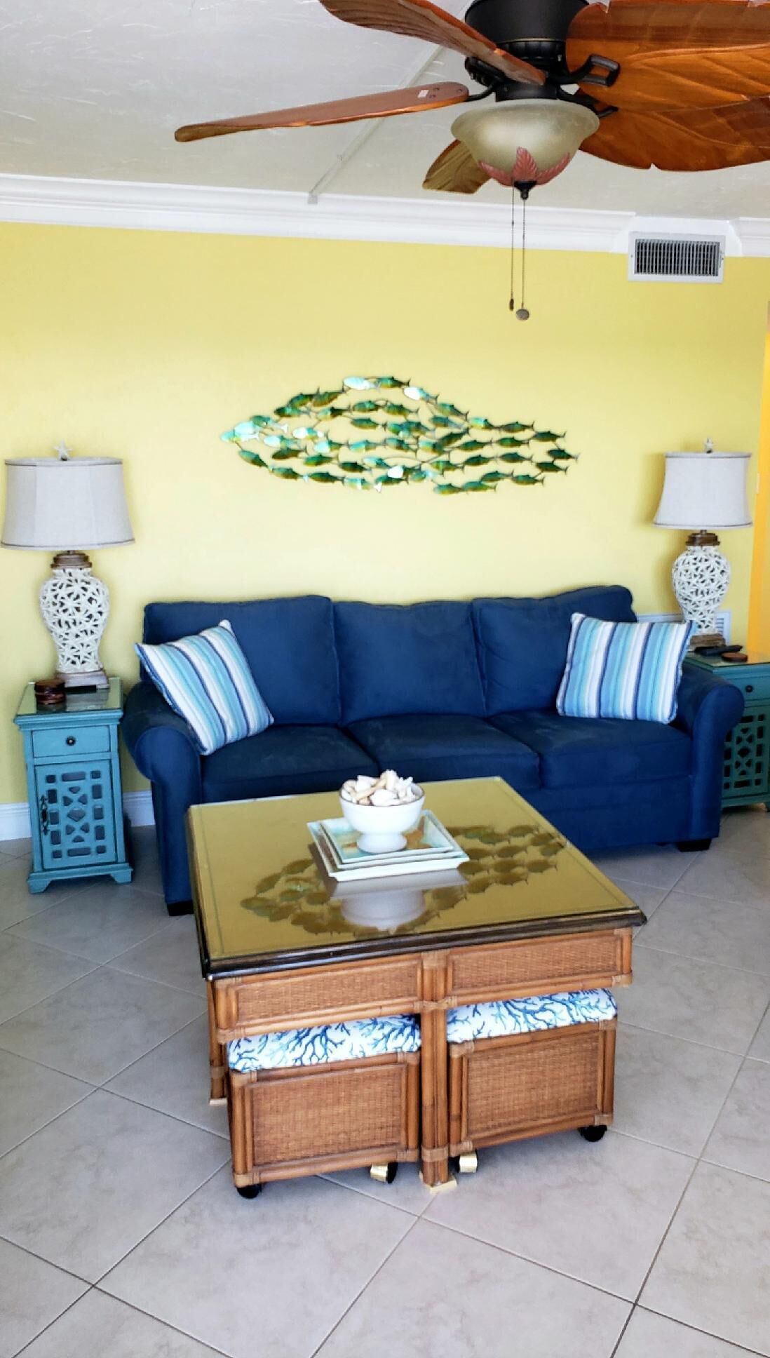 A living room with a blue sofa, a glass-top coffee table, and a decorative wall piece.