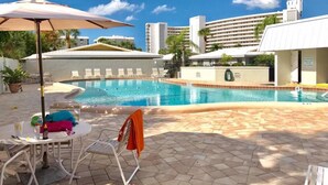 A pool area with lounge chairs, a table with a drink and snacks, and a building in the background. - Crescent Arms Luxurious Gulf front Siesta Key Condo 604S (Siesta Key)
