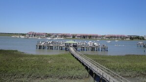 A marina with boats docked, a wooden pier, and a row of buildings with red roofs in the background. - Turtle Bay 15 - Riverfront - Dock & Pool (Folly Beach)