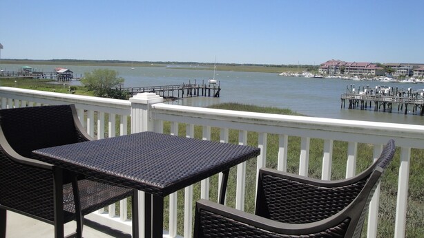 A balcony with wicker furniture overlooking a marina with boats and a dock. - Turtle Bay 15 - Riverfront - Dock & Pool (Folly Beach)