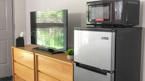 Een kitchenette met een koelkast, een magnetron, een televisie en een houten kastje.