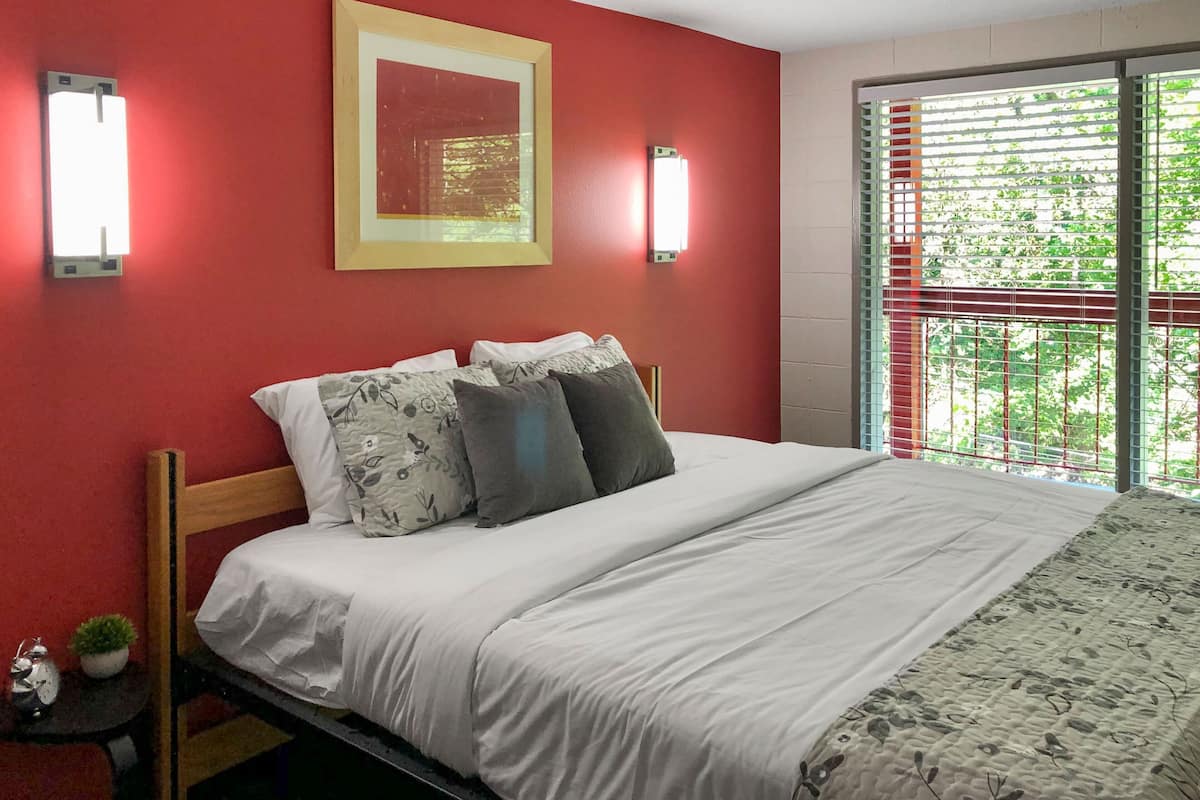 A hotel room with a bed, two wall-mounted lights, a framed picture, and a window with blinds.