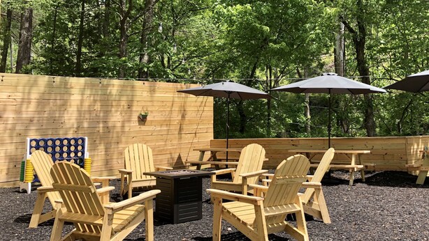 Een terras met houten Adirondack-stoelen en tafels, omgeven door een houten hek en bomen.