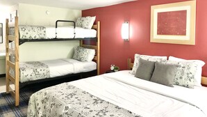 Een kamer met twee stapelbedden, een eenpersoonsbed, een rode muur, een lijst met een afbeelding en een kleine klok op het nachtkastje.
