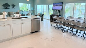A modern kitchen with a dishwasher, a dining area with a table and chairs, and a TV mounted on the wall. - Conch House - Ocean front with dock and pool (Little Torch Key)