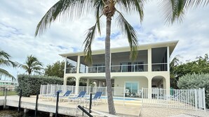 A two-story building with a pool, palm trees, and a dock. - Conch House - Ocean front with dock and pool (Little Torch Key)