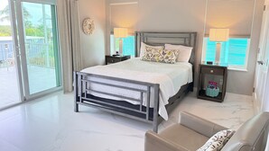 A bedroom with a bed, two bedside tables, a chair, a window with blinds, and an air conditioning unit. - Conch House - Ocean front with dock and pool (Little Torch Key)
