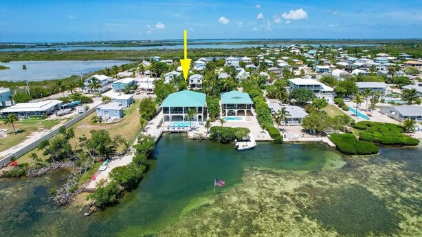 An aerial view of a coastal residential area with houses, a clear water body, and a flag. - Conch House - Ocean front with dock and pool (Little Torch Key)