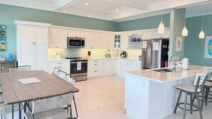 A modern kitchen with white cabinetry, a central island, stainless steel appliances, and pendant lighting. - Conch House - Ocean front with dock and pool (Little Torch Key)