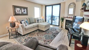 A living room with a sectional sofa, a patterned rug, a piano, and a large window with a view.
