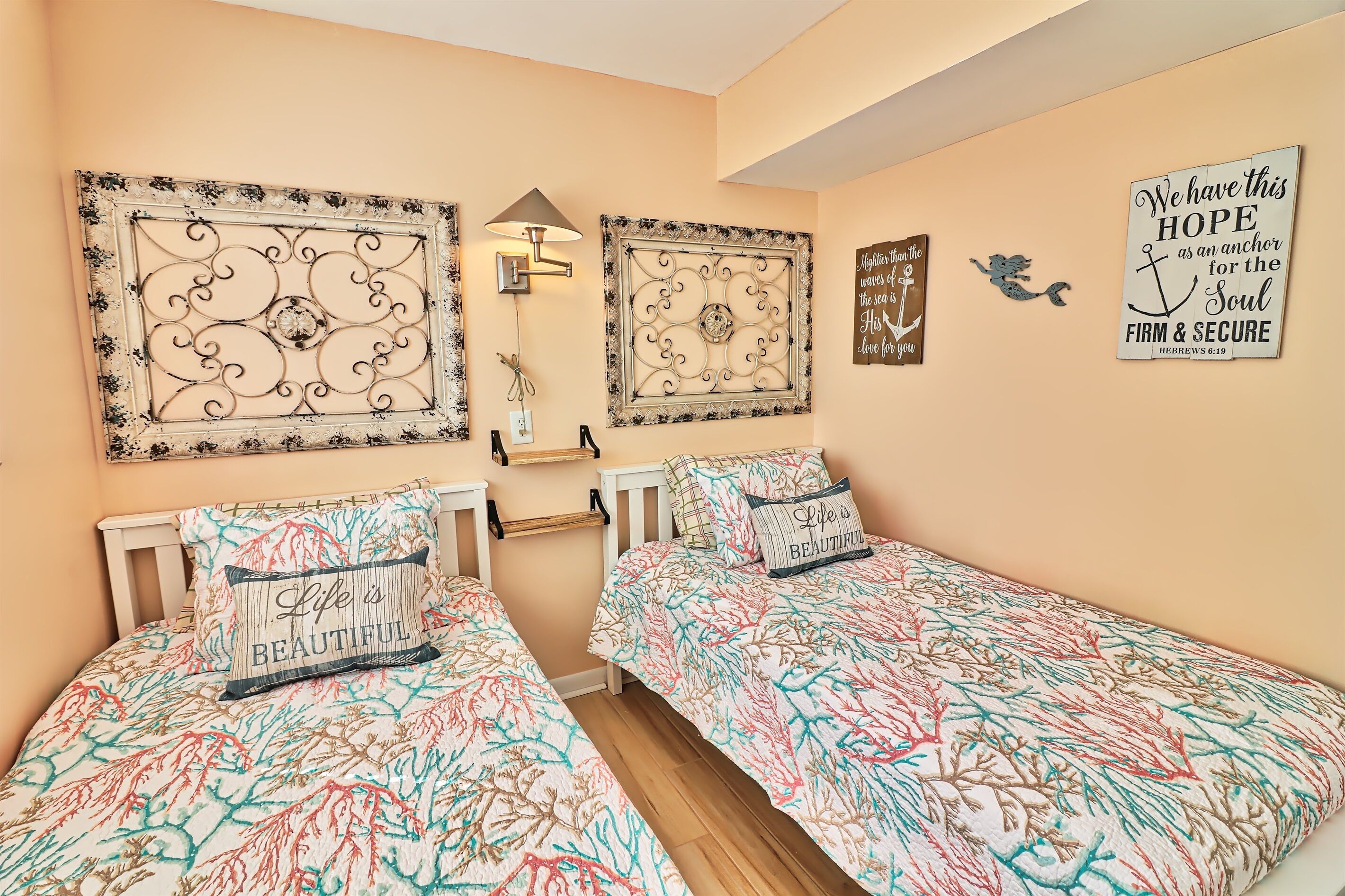 Une chambre avec deux lits simples, une table de chevet, une lampe fixée au mur et des œuvres d’art décoratives accrochées au mur.