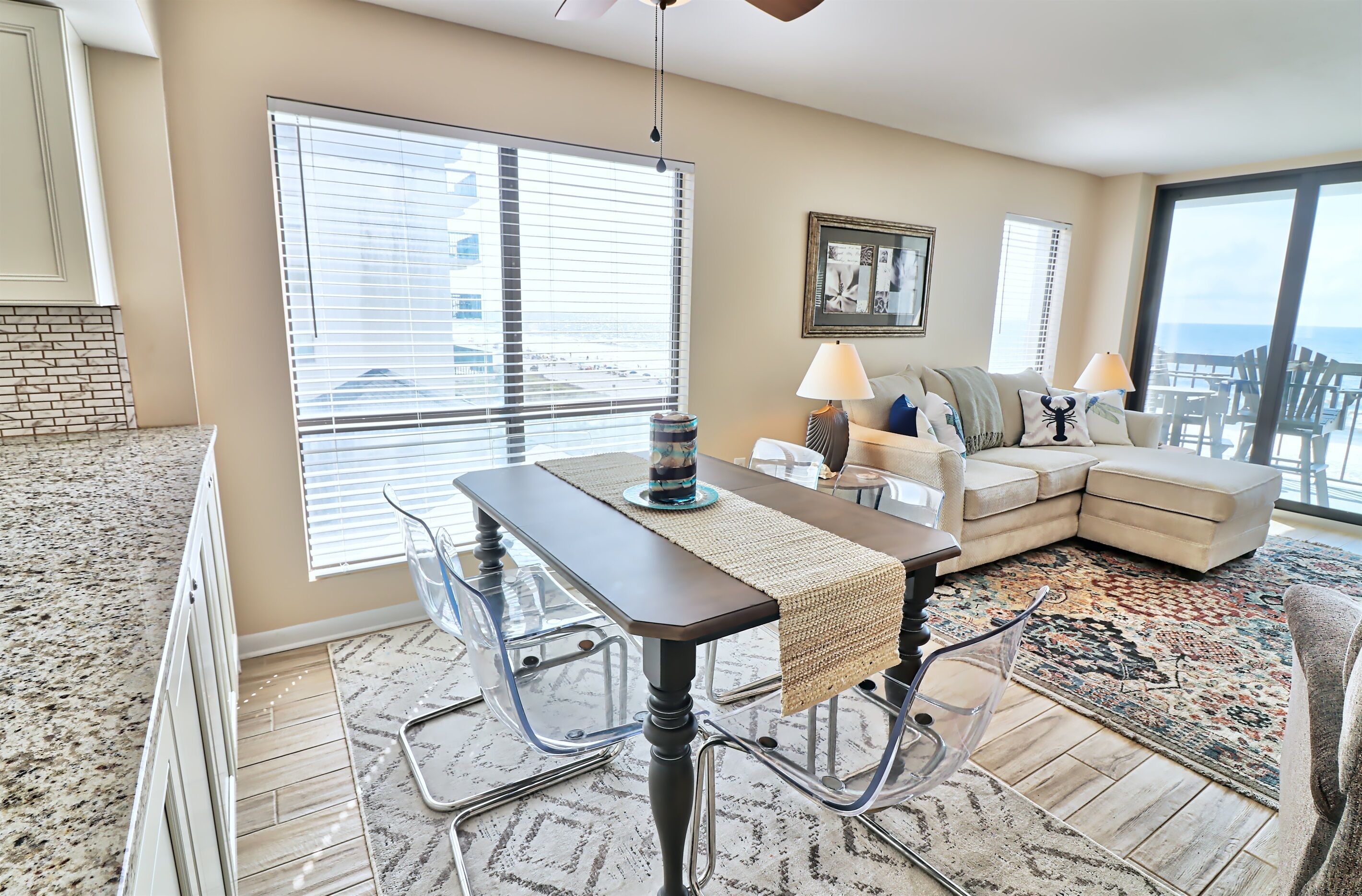 A spacious living room with a large window, a dining table, a sofa, and a view of the ocean.