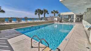 A swimming pool with a metal ladder, lounge chairs, and palm trees in the background.