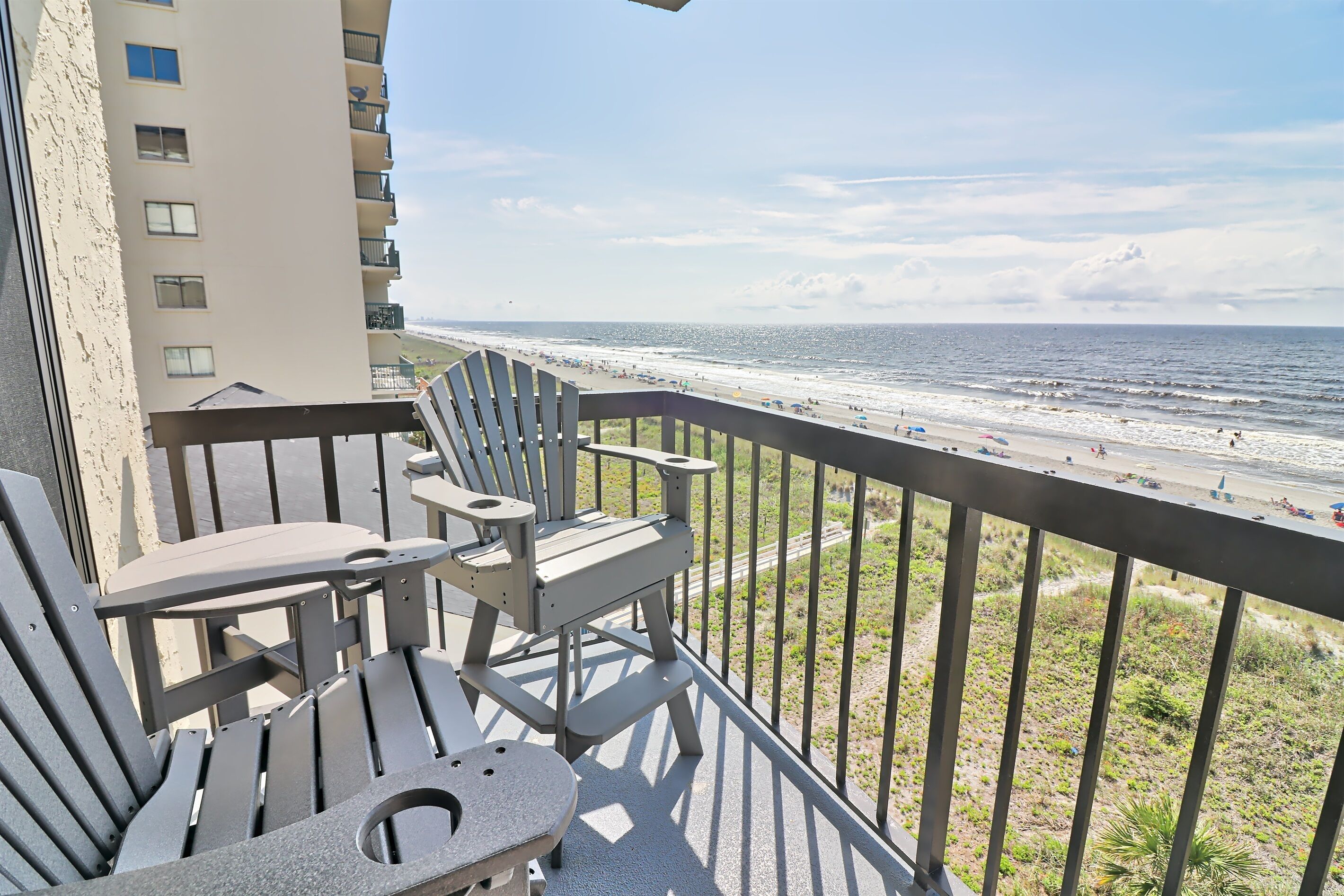 Een balkon met uitzicht op het strand, met een tafel en twee stoelen.
