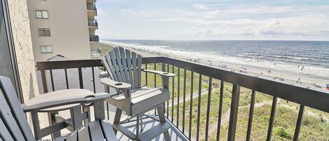 Een balkon met uitzicht op het strand, met een tafel en twee stoelen.