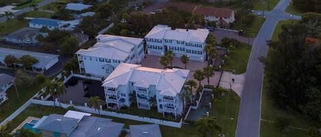 An aerial view of a residential area with a large white building complex, a marina, and a sunset in the background.