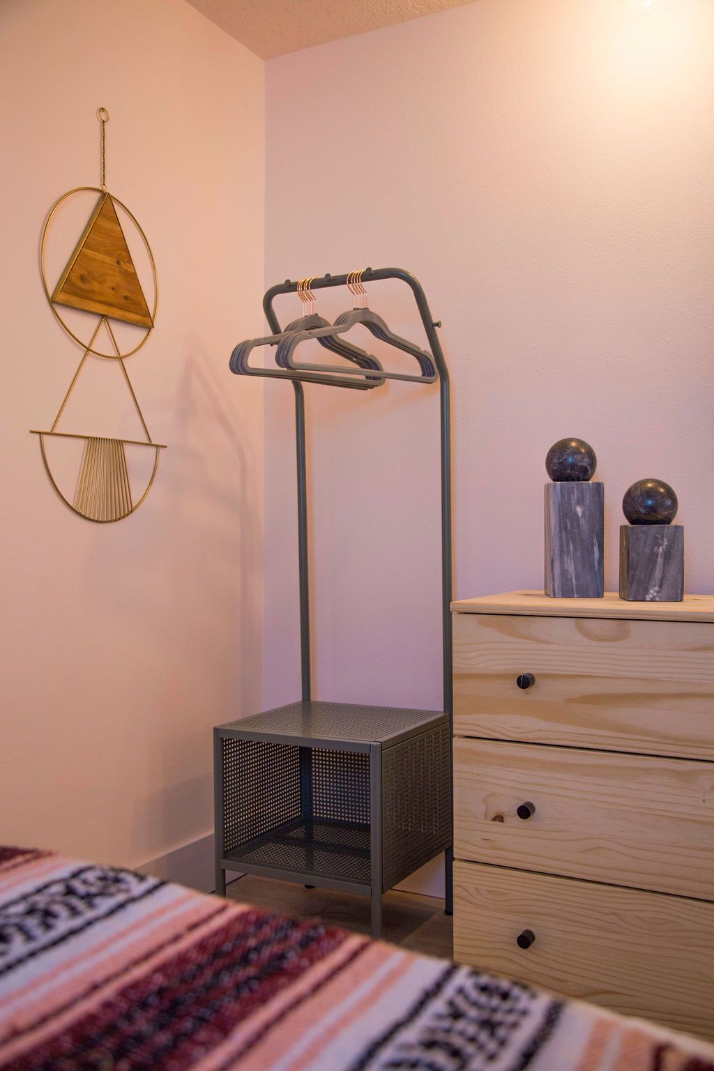 A bedroom with a bed, a metal drying rack, a wooden dresser, and wall decorations.