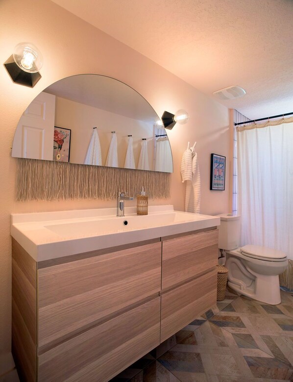 A modern bathroom with a large mirror, a wooden vanity, a toilet, and a shower curtain. - Stylish & Eclectic Modern 2/2 Apt - WeAreGrateful (South Pasadena)