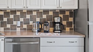 Eine Küche mit weißen Schränken, einer gefliesten Spritzschutzwand, einer Kaffeemaschine, einem Wasserkocher und einem Geschirrspüler.