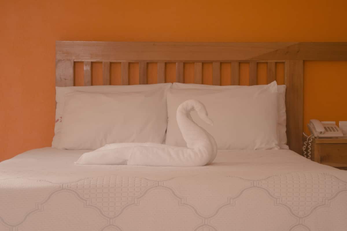 Una cama con cabecera de madera, almohadas blancas y una toalla con forma de cisne.