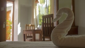 A swan-shaped towel on a bed in a room with a wooden chair and a window with curtains.