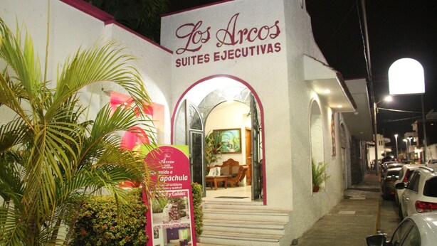 A building with a sign reading "Los Arcos Suites Ejecutivas" and a visible entrance.